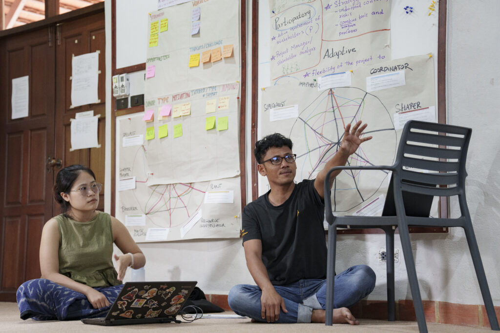 two people sitting on the floor in front of white board with may post-its and other notes on top