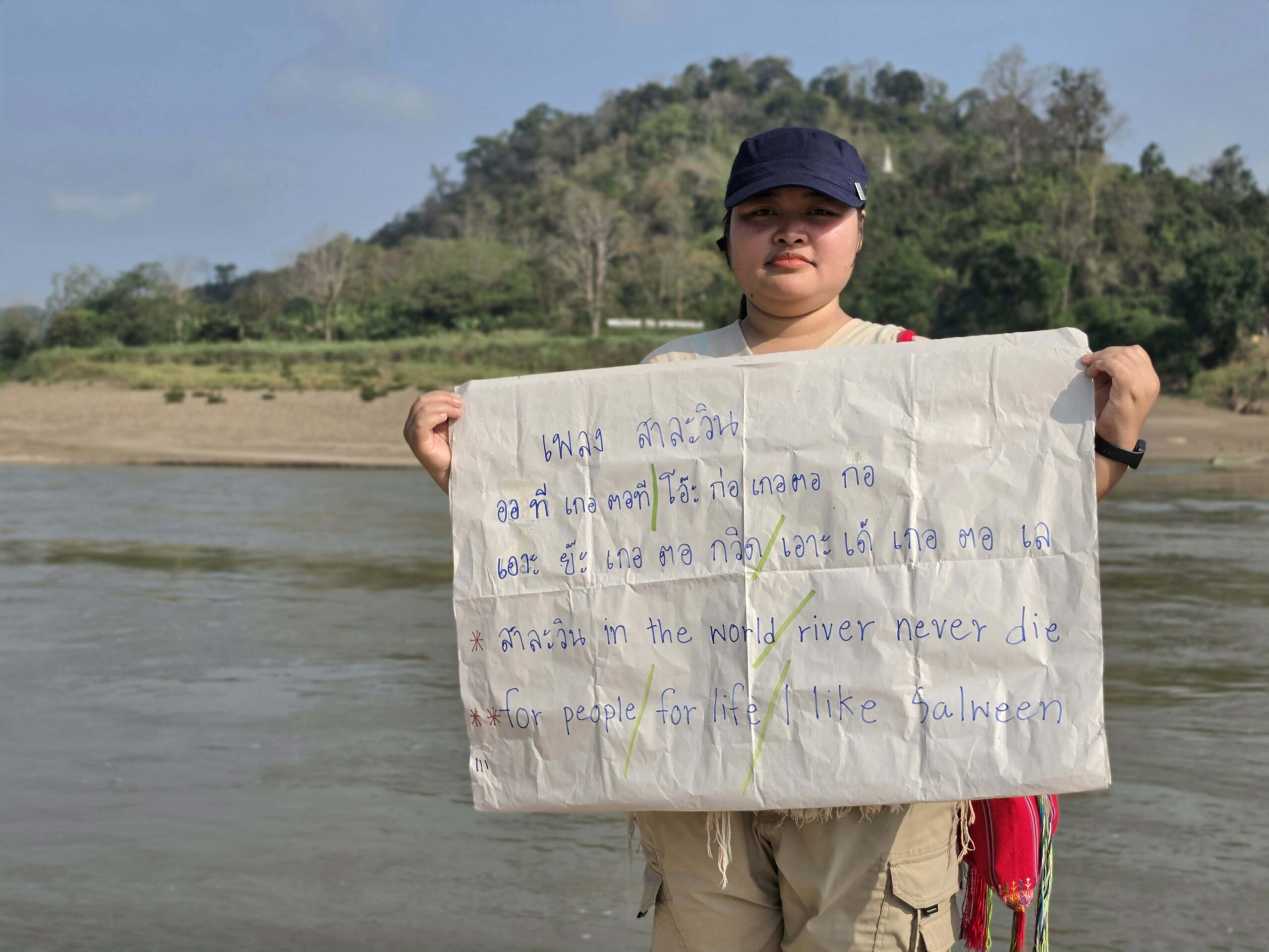 person holding a sign with river behind