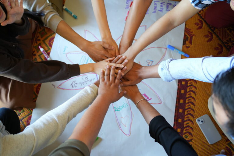 hands on top of one another with people around in a circle